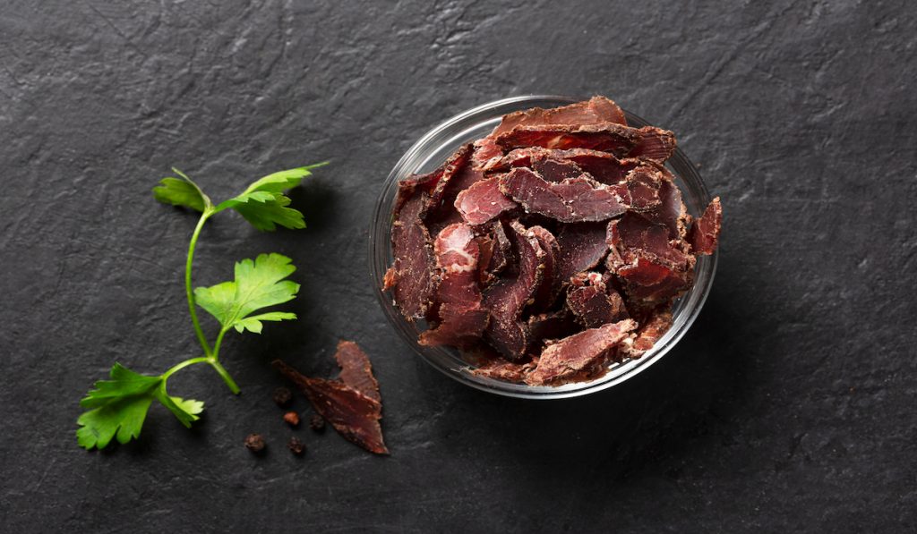 bowl of dry beef jerky and a small branch of parsley