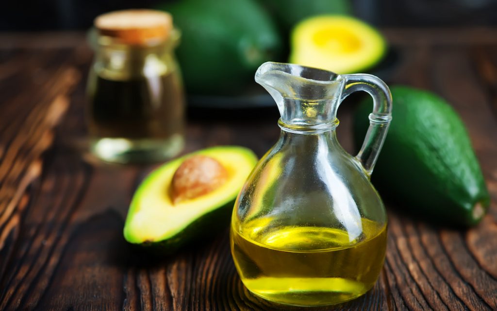 avocado oil in jar and fresh slice avocado