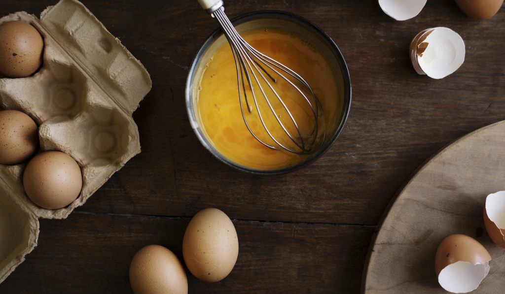 beaten eggs and whole egg on tray wooden table 