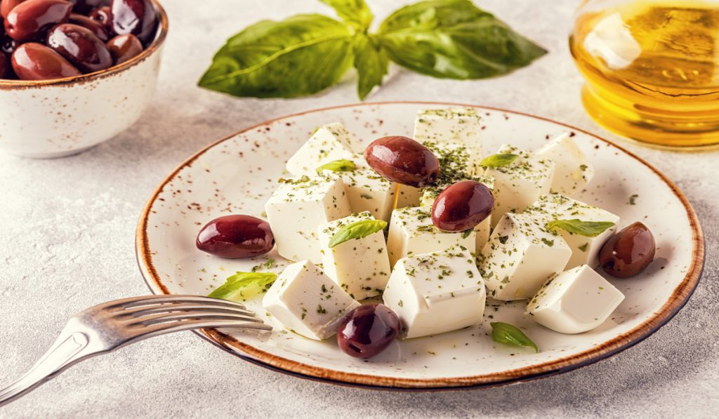 feta cheese with olives and oregano on a white plate