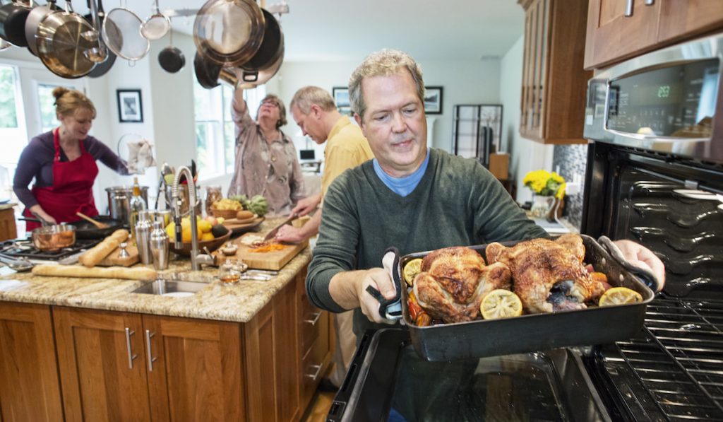 old man pull roast chickens out of the oven for home party preparation