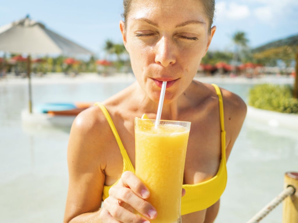 sexy woman drinking mango juice in yellow body swim suit 