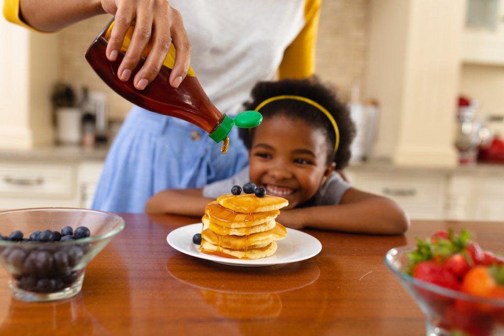 mom pouring maple syrup over the little girl's pancake