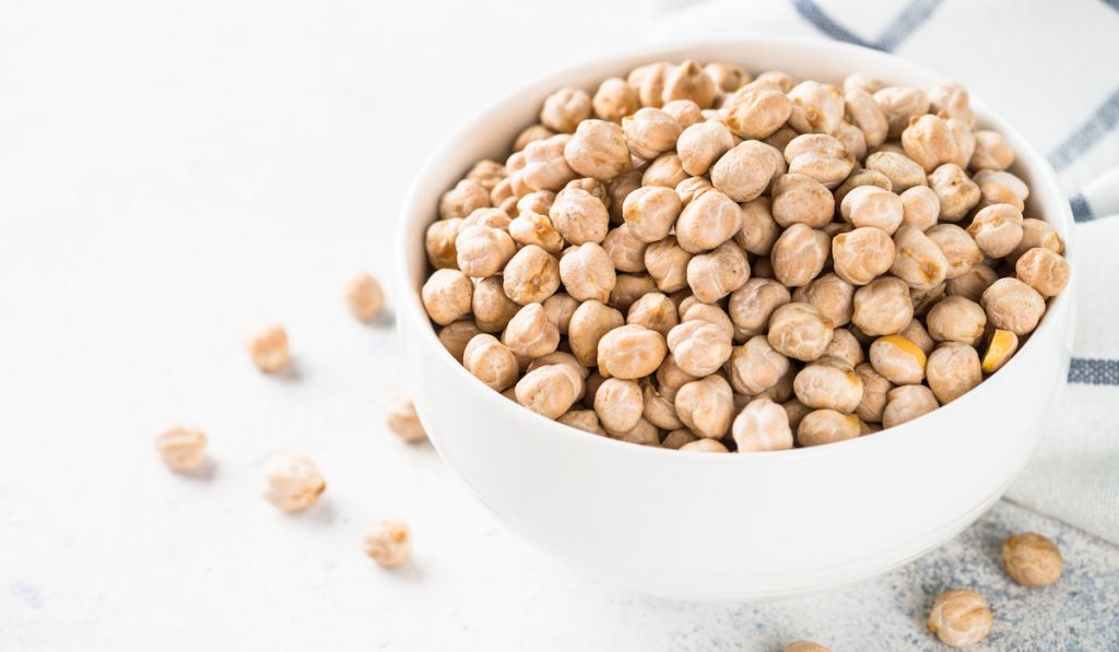 Chickpeas in white bowl at light kitchen table.
